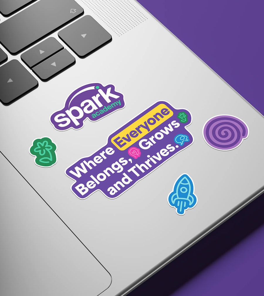 Spark Academy sticker designs mocked up on a laptop lid