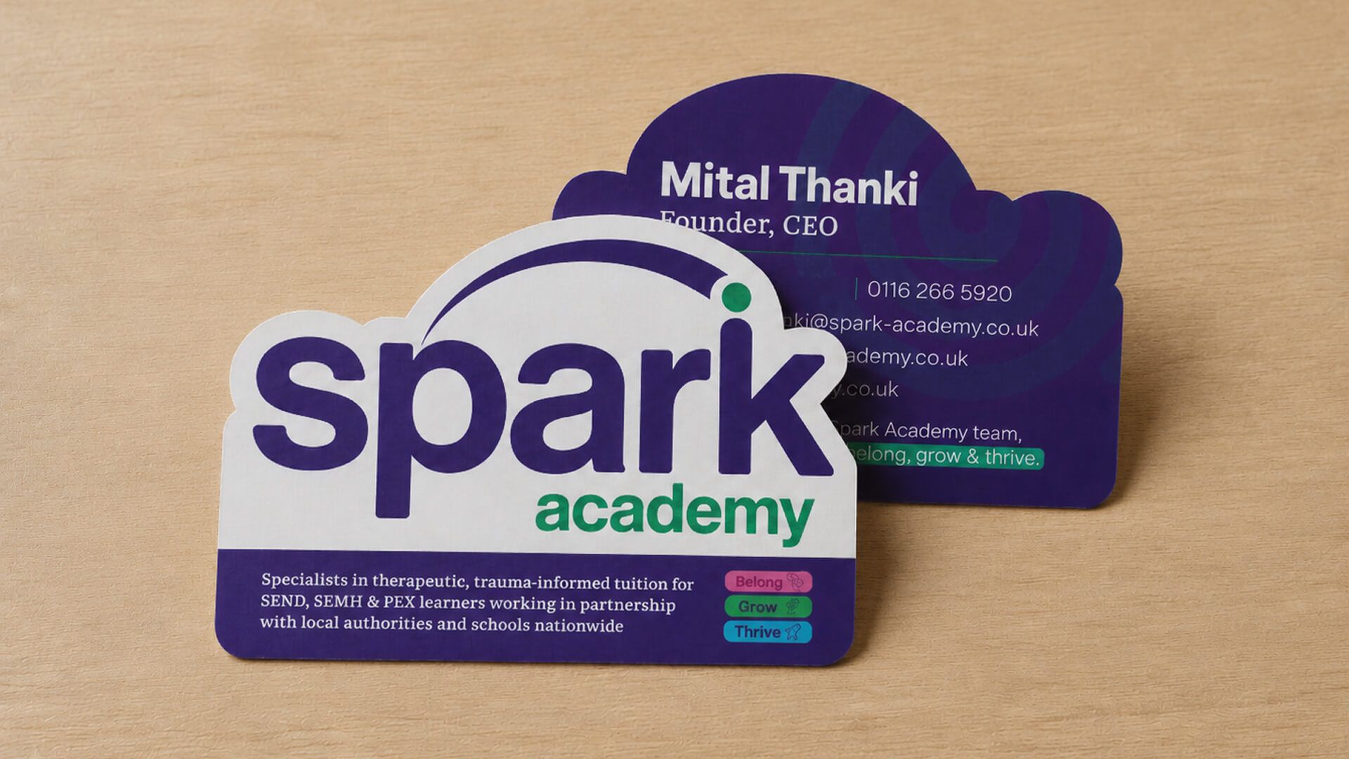 Spark Academy die-cut business card design on a wooden desk